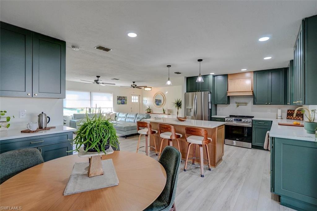 Kitchen with light wood-type flooring, stainless steel appliances, sink, decorative light fixtures, and a center island