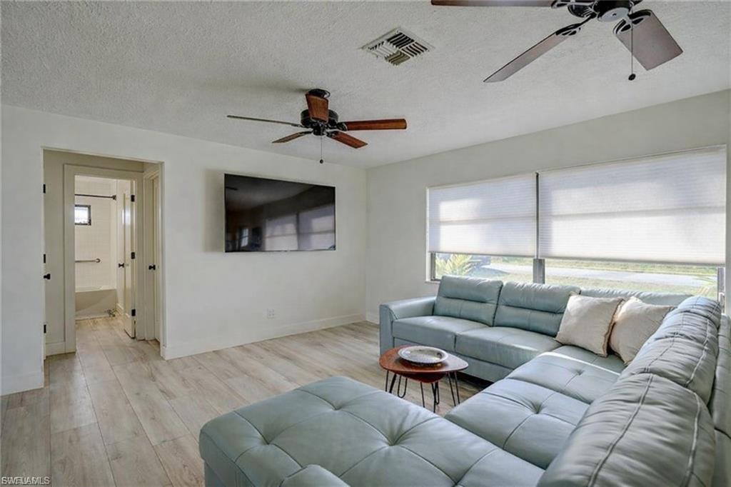 Living room with ceiling fan, a textured ceiling, and wood finished floors