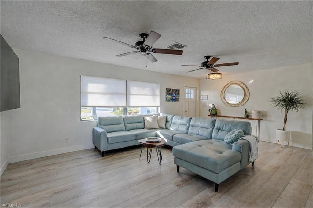Living area with a textured ceiling, light wood-style floors, and a ceiling fan