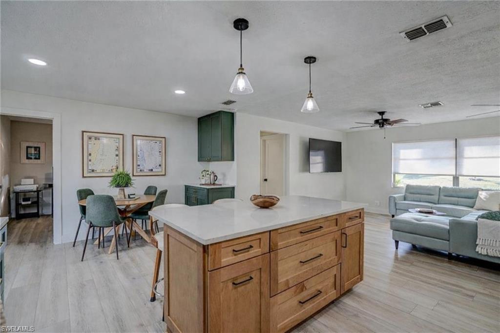 Kitchen with hanging light fixtures, light wood-style flooring, open floor plan, a kitchen island, and light stone counters