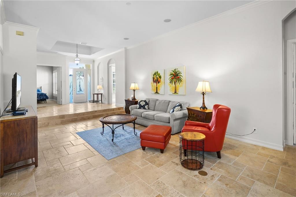 Living room featuring arched walkways, stone tile floors, ornamental molding, and a tray ceiling