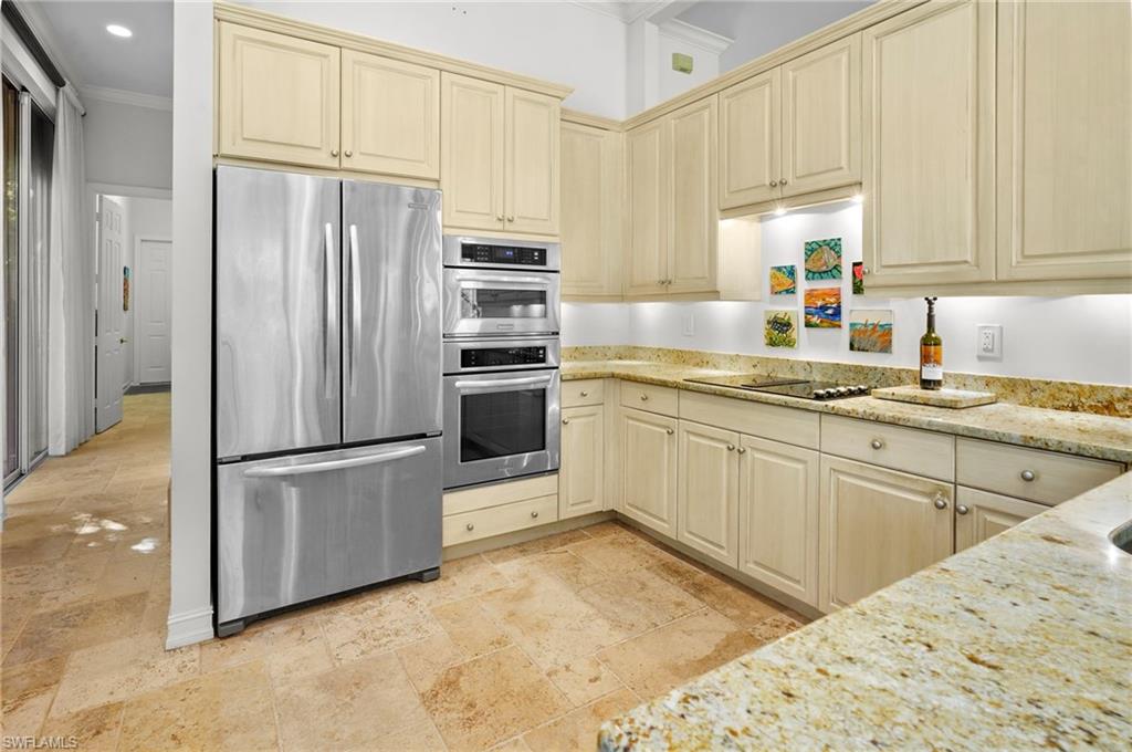 Kitchen with stainless steel appliances, light stone countertops, ornamental molding, cream cabinets, and stone tile flooring