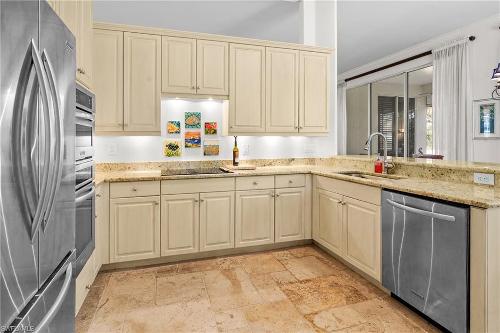 Kitchen featuring stainless steel appliances, cream cabinetry, light stone counters, a peninsula, and stone tile flooring