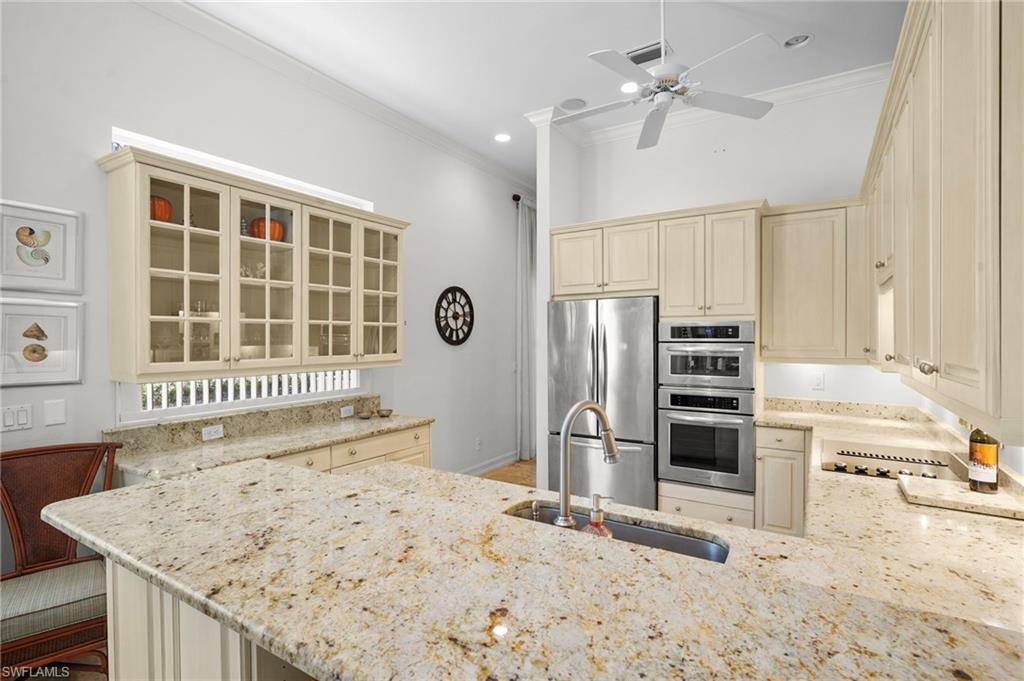 Kitchen with glass fronted cabinets, stainless steel appliances, ornamental molding, cream cabinets, and light stone countertops