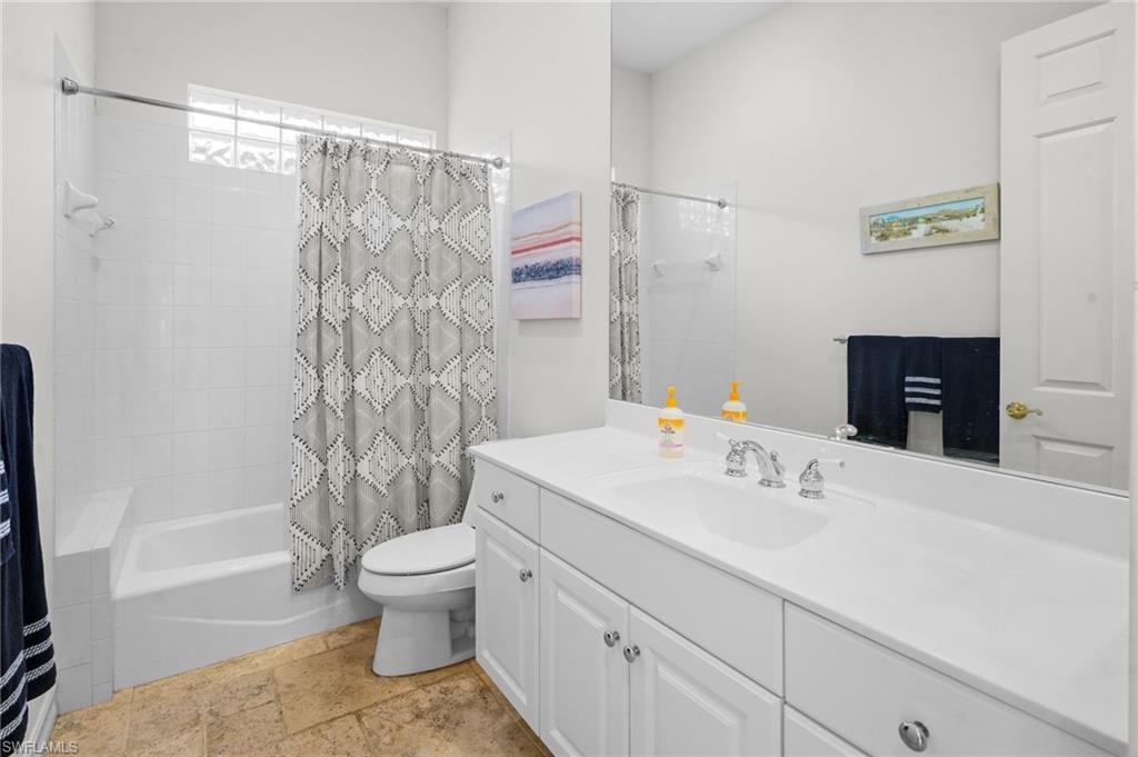 Full bathroom featuring shower / tub combo with curtain, vanity, and stone tile flooring