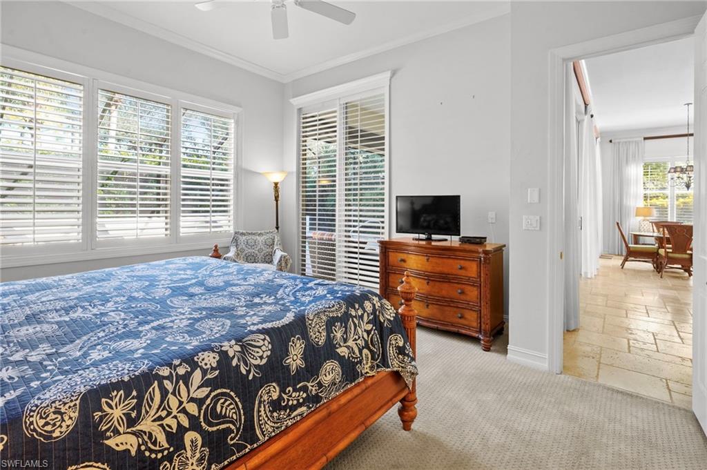 Carpeted bedroom featuring stone tile floors, crown molding, and a ceiling fan