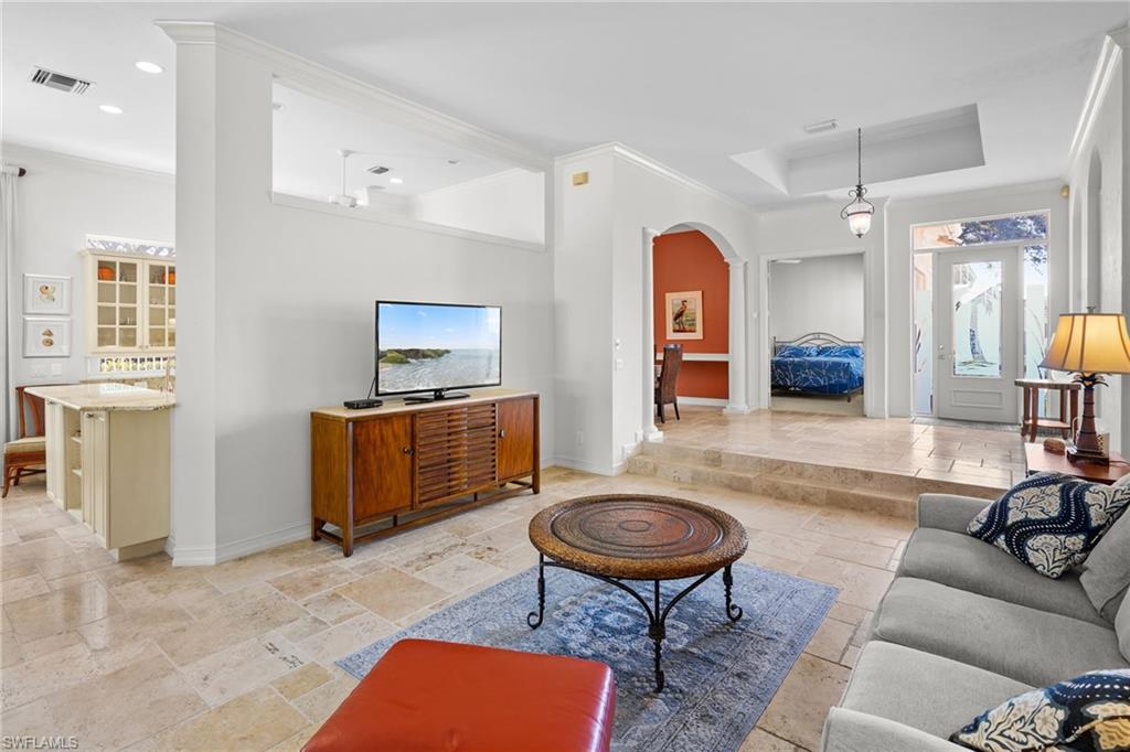 Living room with stone tile flooring, arched walkways, crown molding, and a tray ceiling