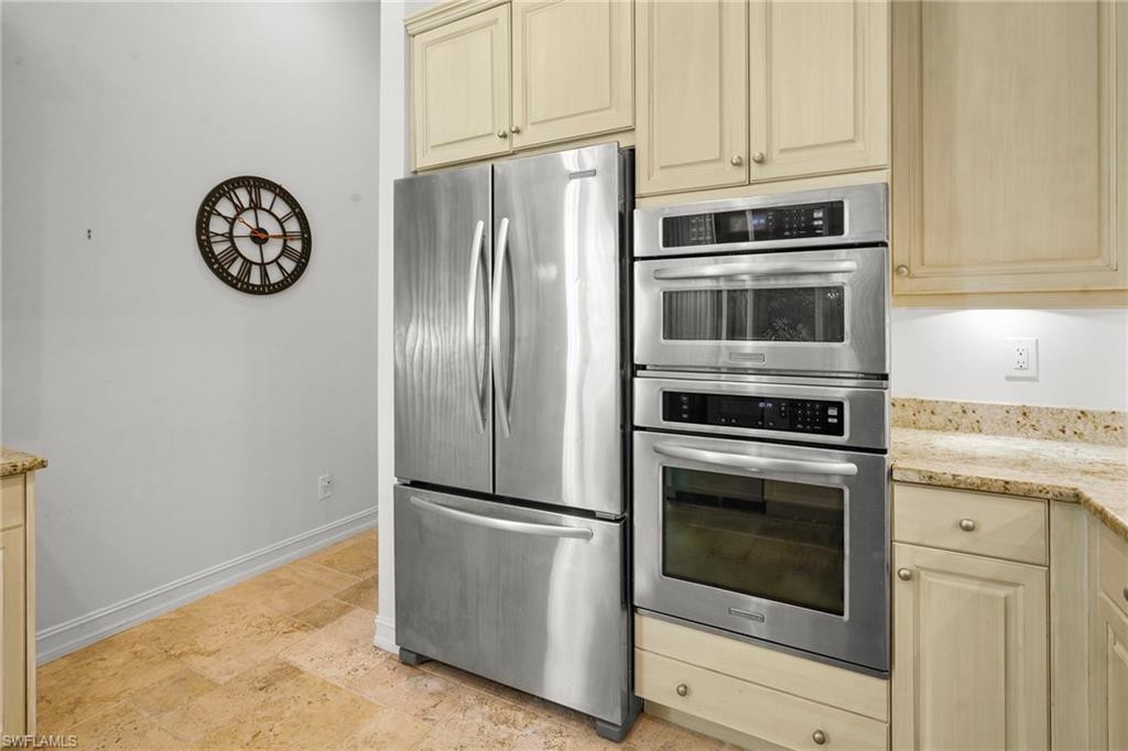 Kitchen with stainless steel appliances, light stone counters, light wood finish cabinets, light stone finish floors, and cream cabinets