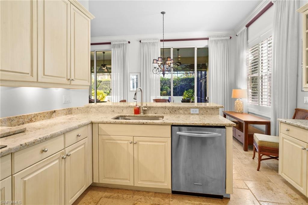 Kitchen featuring light stone countertops, cream cabinetry, stainless steel dishwasher, and suspended lighting
