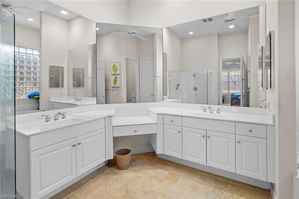 Bathroom with a stall shower, two vanities, stone tile flooring, connected bathroom, and ceiling fan