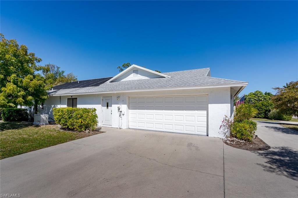 View of front facade of large garage with circular driveway, a shingled roof, solar panels.