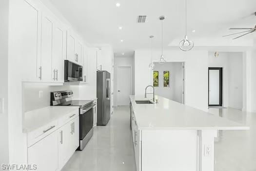 Kitchen with stainless steel appliances, white cabinetry, concrete floors, a large island with sink, and hanging light fixtures