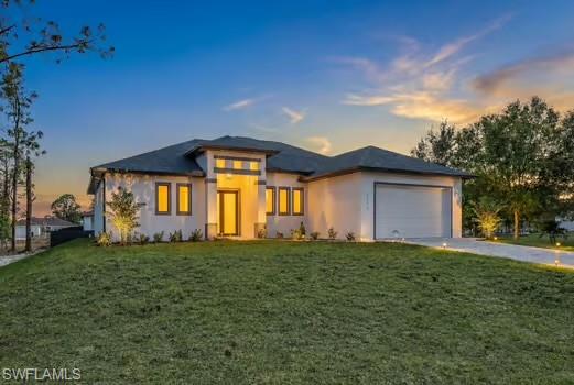 Prairie-style house featuring a front lawn, stucco siding, driveway, and a garage