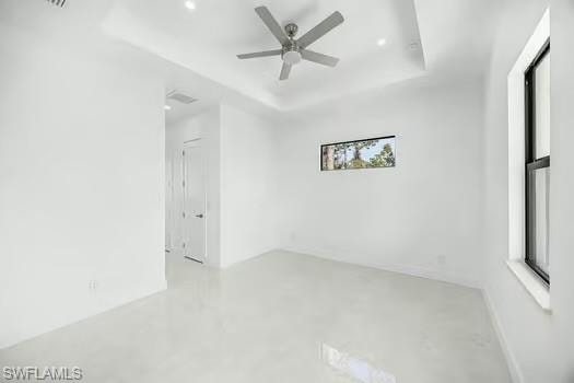 Unfurnished room with finished concrete floors, a tray ceiling, and ceiling fan