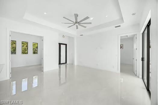 Unfurnished room with finished concrete floors, ceiling fan, and a tray ceiling