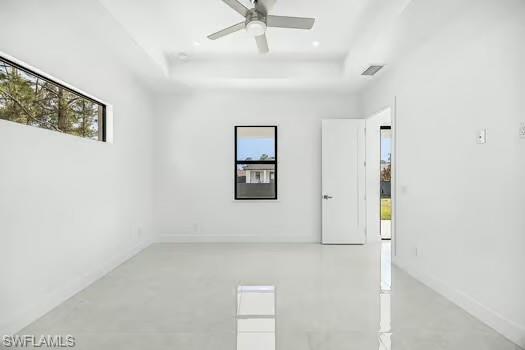 Empty room with plenty of natural light, a ceiling fan, finished concrete flooring, and a tray ceiling