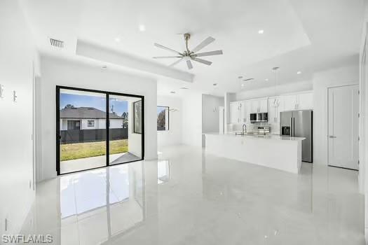 Unfurnished living room featuring a ceiling fan, a raised ceiling, and finished concrete floors