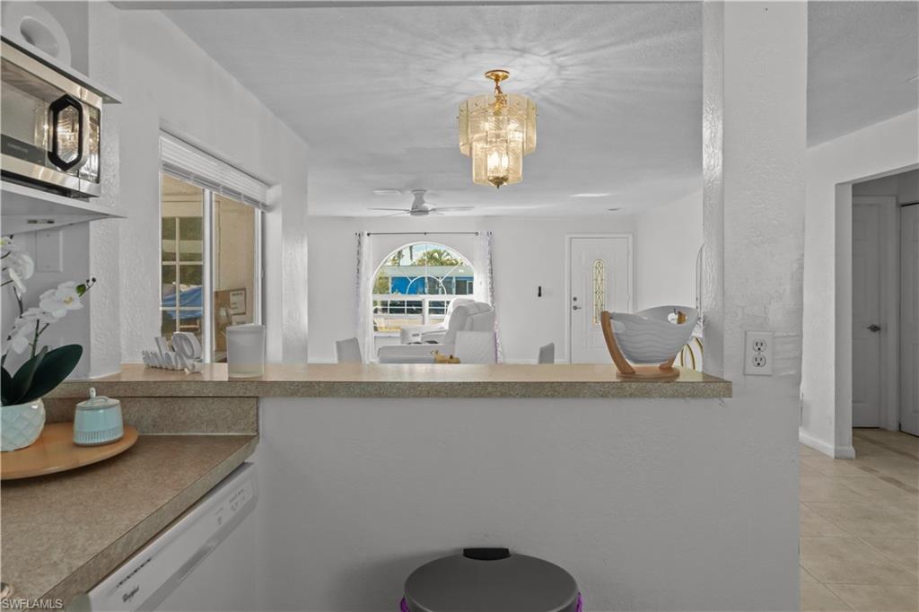 Kitchen with stainless steel microwave, dishwasher, a ceiling fan, hanging lights, and light countertops