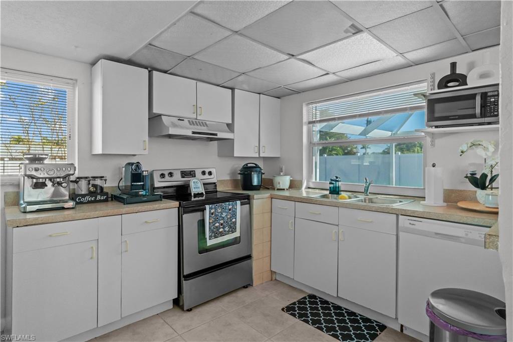 Kitchen featuring stainless steel appliances, light countertops, white cabinets, healthy amount of natural light, and a paneled ceiling