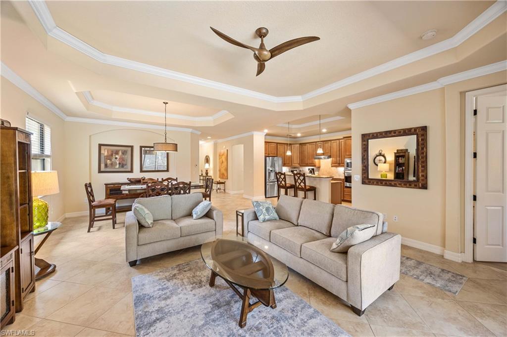 Living area featuring a ceiling fan, a raised ceiling, light tile patterned floors, and baseboards