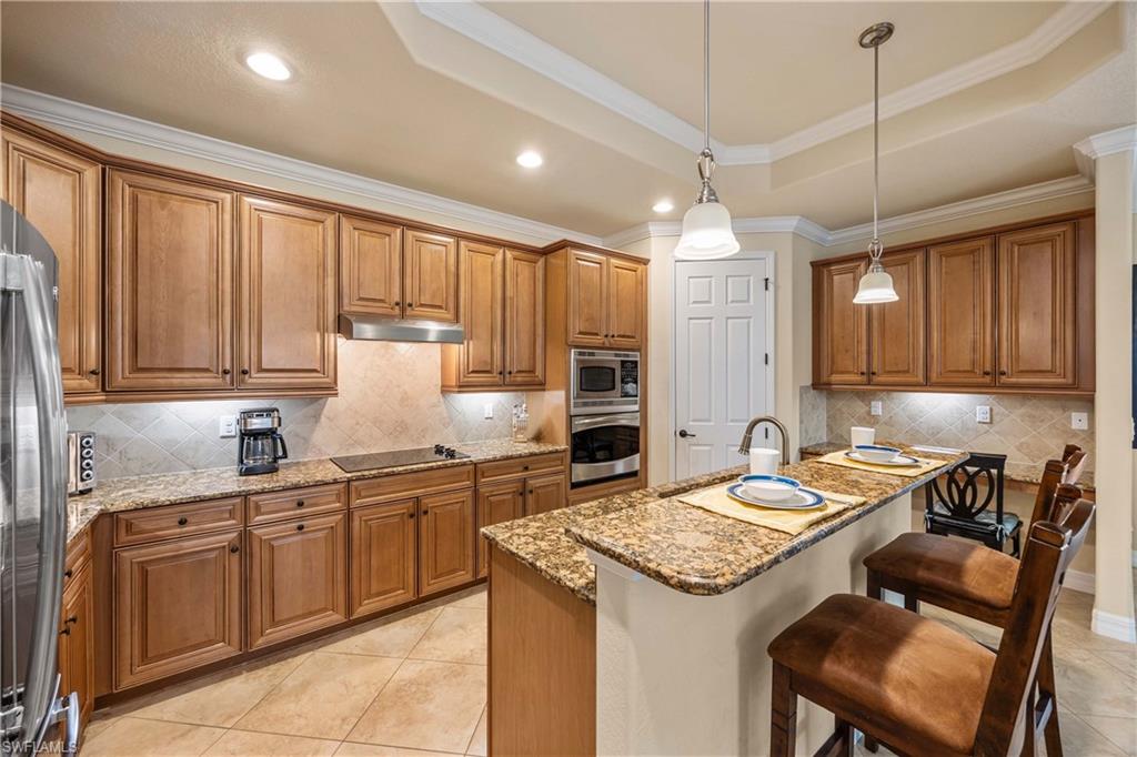 Kitchen featuring a tray ceiling, brown cabinetry, under cabinet range hood, and stainless steel appliances