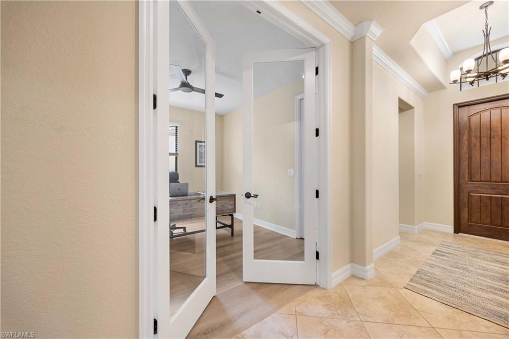 Entrance foyer featuring light tile patterned flooring, baseboards, crown molding, and ceiling fan with notable chandelier