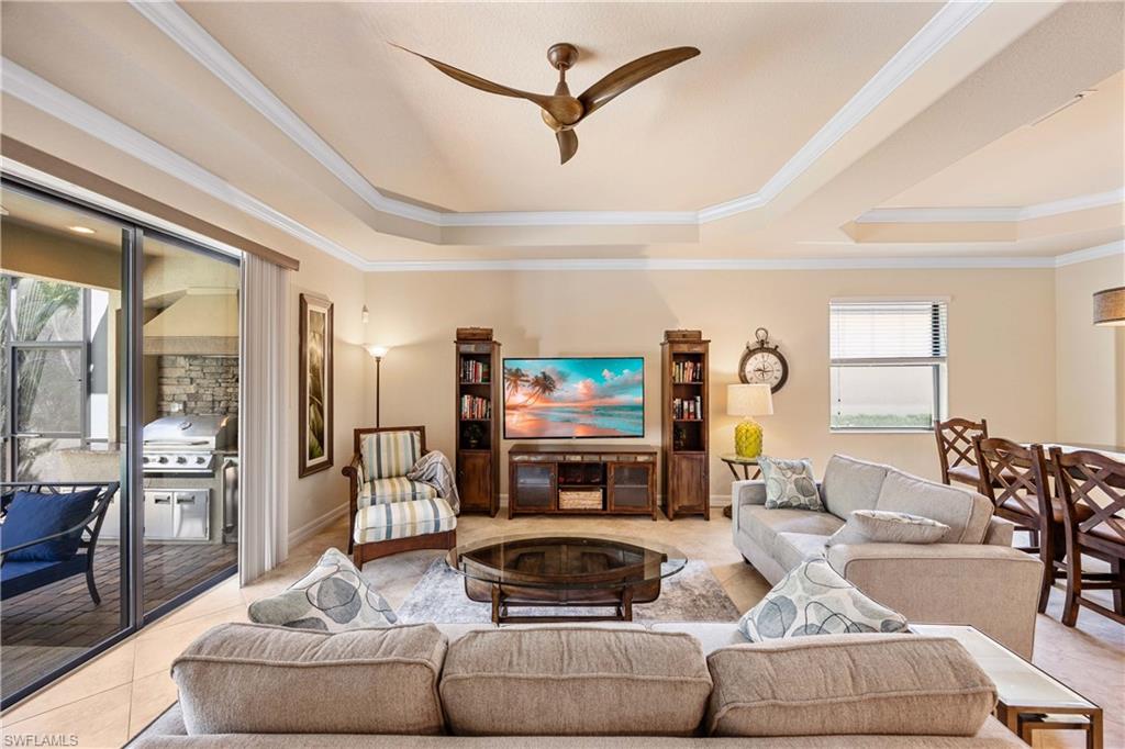 Living room featuring ornamental molding, a raised ceiling, light tile patterned floors, and ceiling fan