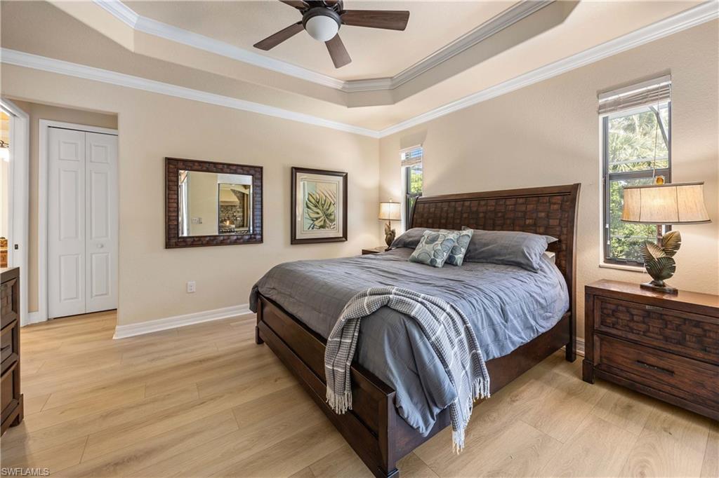 Bedroom featuring a tray ceiling, multiple windows, light wood-style floors, and ornamental molding