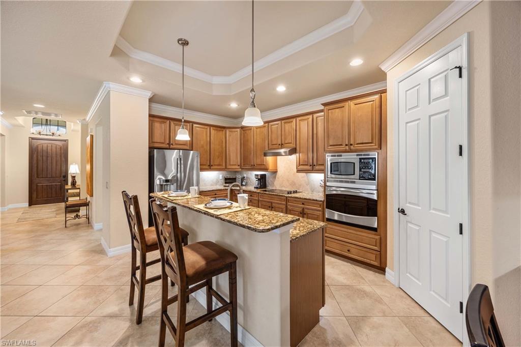 Kitchen featuring a raised ceiling, stainless steel appliances, under cabinet range hood, and brown cabinets