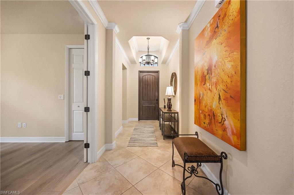 Entrance foyer featuring light tile patterned flooring, a notable chandelier, crown molding, baseboards, and arched walkways