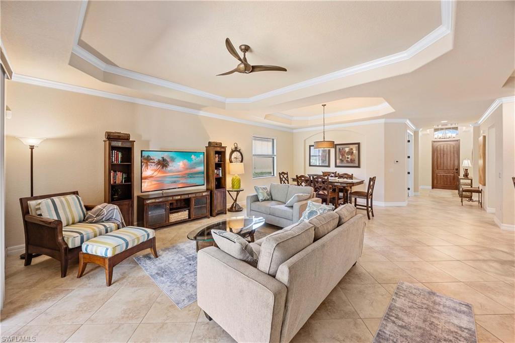 Living room featuring crown molding, baseboards, ceiling fan, a raised ceiling, and light tile patterned floors