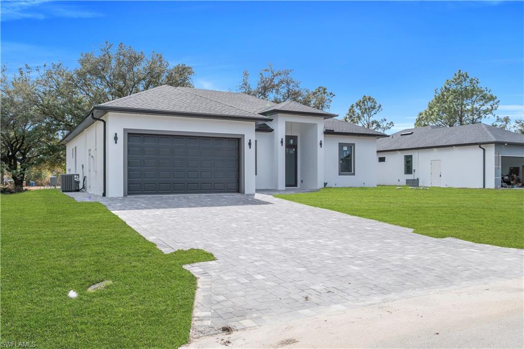 Prairie-style home with a front yard, decorative driveway, stucco siding, and roof with shingles