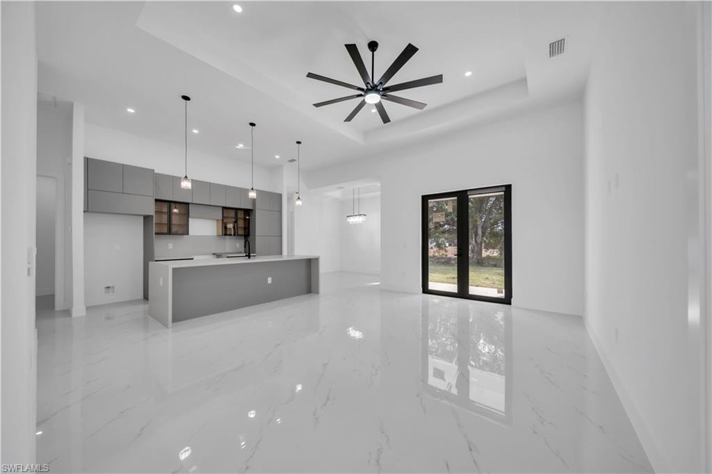 Unfurnished living room featuring light marble finish floors, recessed lighting, a raised ceiling, and a ceiling fan