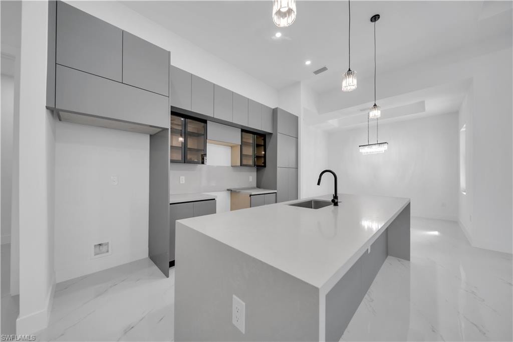 Kitchen with modern cabinets, gray cabinetry, a center island with sink, hanging light fixtures, and light marble finish floors