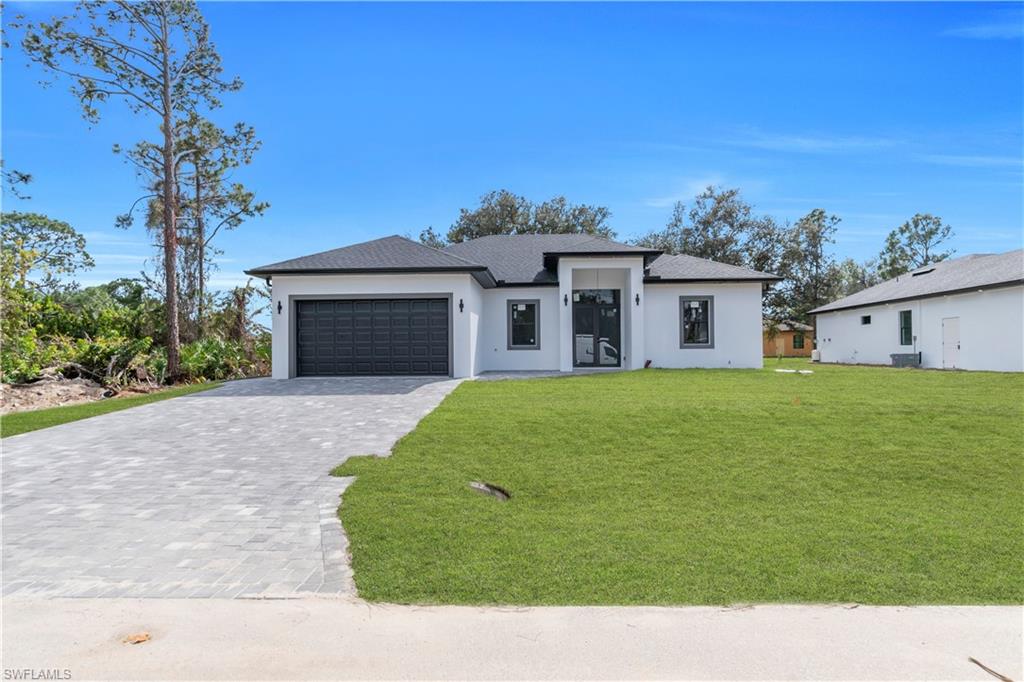 View of front of home with decorative driveway, stucco siding, a front yard, a garage, and roof with shingles