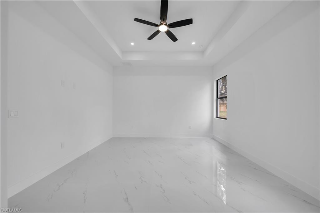 Empty room featuring a ceiling fan, light marble finish flooring, recessed lighting, and a tray ceiling