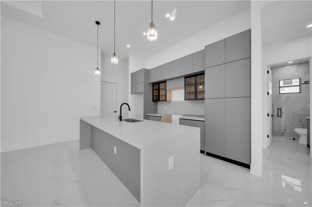 Kitchen featuring gray cabinets, modern cabinets, decorative light fixtures, light marble finish floors, and light stone counters