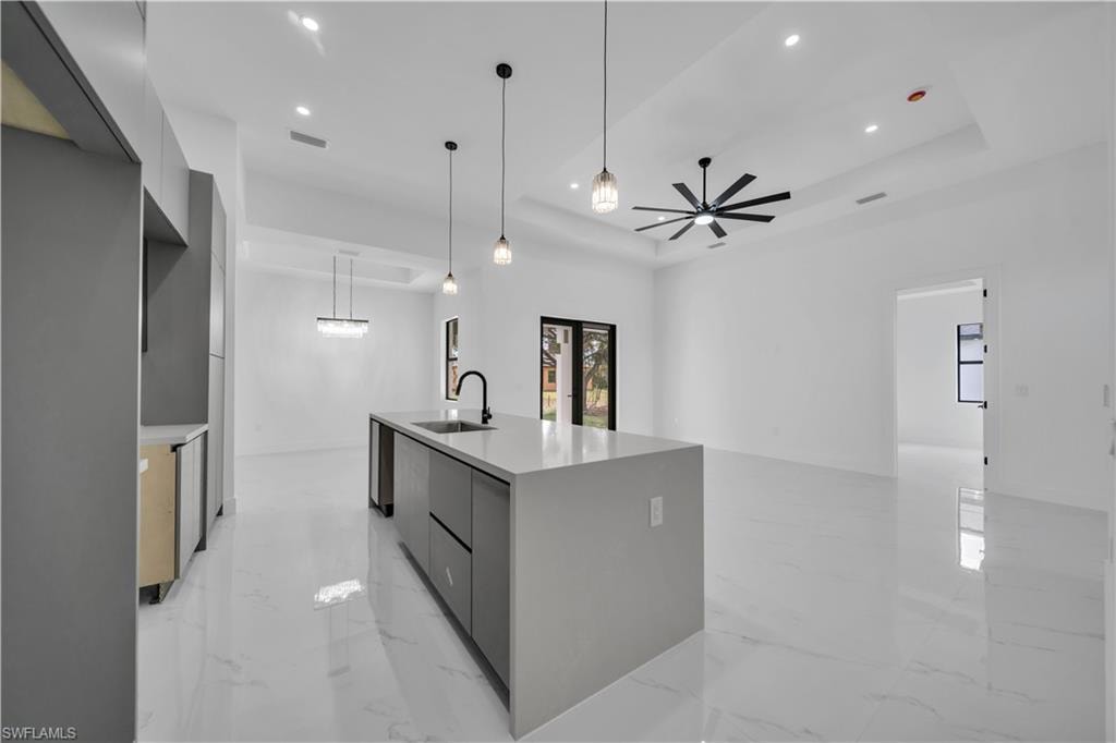 Kitchen with modern cabinets, an island with sink, light marble finish floors, and light stone countertops