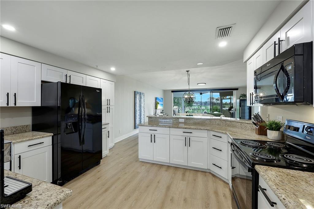 Kitchen with black appliances, white cabinets, light stone counters, and a peninsula