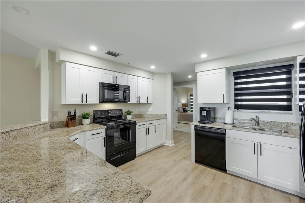 Kitchen featuring black appliances, white cabinetry, light stone countertops, and recessed lighting