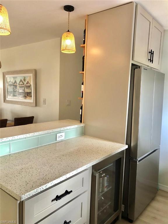 Kitchen featuring white cabinets, light stone countertops, wine cooler, freestanding refrigerator, and open shelves
