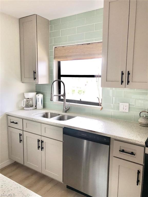 Kitchen with dishwasher, light stone counters, light wood-style flooring, and decorative backsplash