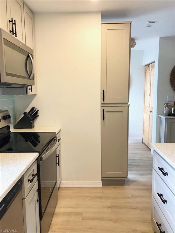 Kitchen with stainless steel appliances, light stone countertops, light wood-type flooring, gray cabinetry, and decorative backsplash