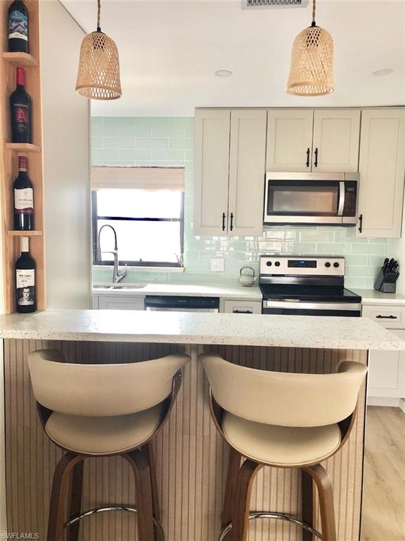 Kitchen with a kitchen breakfast bar, stainless steel appliances, light stone countertops, pendant lighting, and backsplash