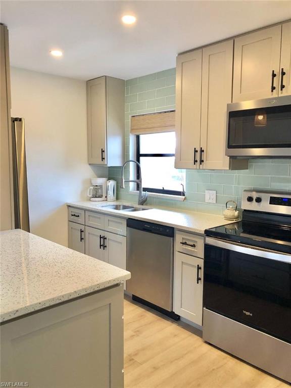 Kitchen with stainless steel appliances, light wood-style floors, light stone counters, backsplash, and recessed lighting