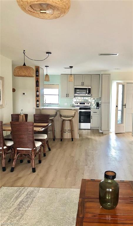 Kitchen featuring decorative backsplash, stainless steel appliances, pendant lighting, a kitchen bar, and light wood-type flooring