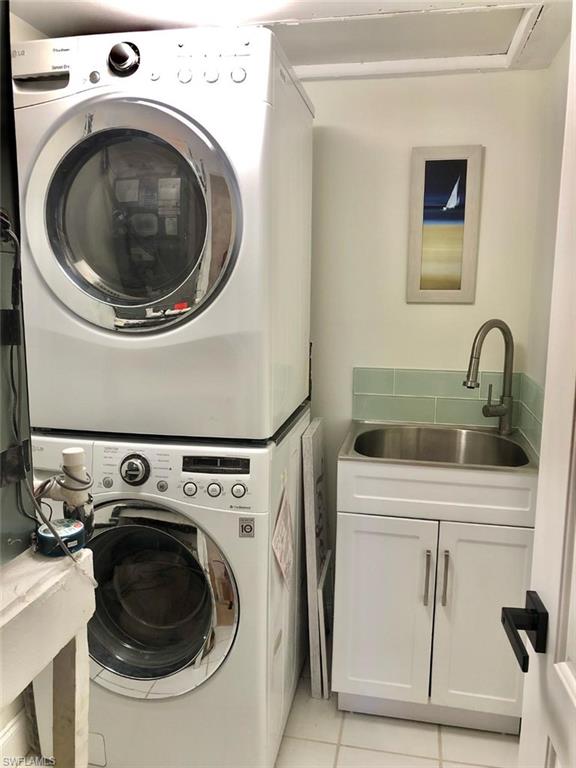 Laundry area with stacked washing machine and dryer, light tile patterned floors, and cabinet space