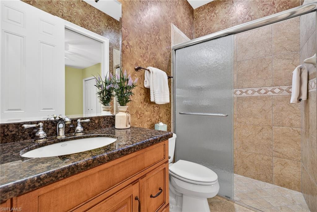Full bathroom featuring vanity, a tile shower, and wallpapered walls