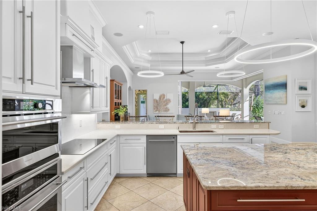 Kitchen featuring light stone countertops, stainless steel appliances, ceiling fan, decorative light fixtures, and two tone cabinetry