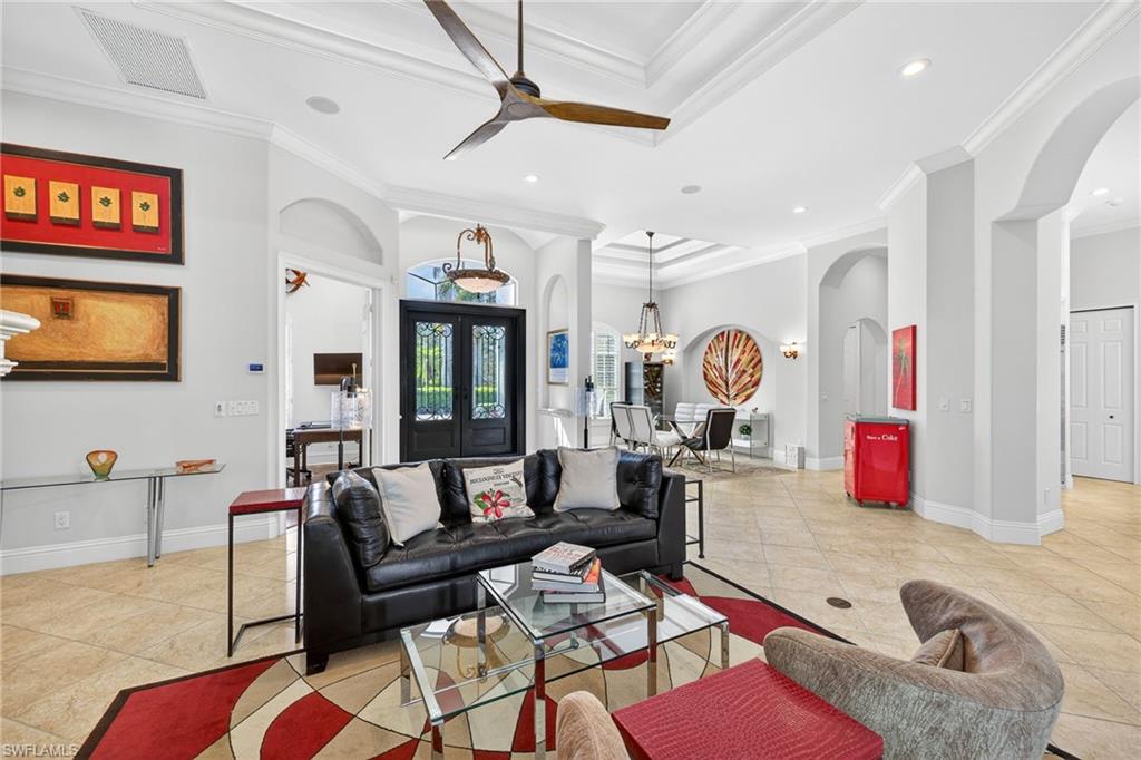 Living room featuring ceiling fan, a chandelier, a high ceiling, arched walkways, and crown molding